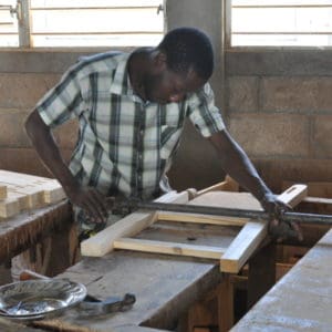 A student practicing constructing a chair in the carpentry workshop of Les Cayes